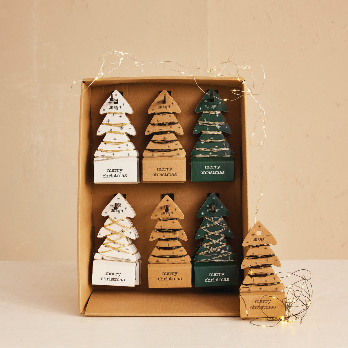 Set of wooden Christmas tree ornaments in a box with 'merry christmas' text on a beige background.