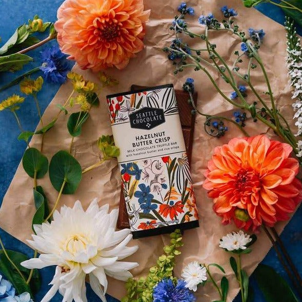 Seattle Chocolate Hazelnut Buttercrisp Truffle Bar on craft paper with clue and orange flowers