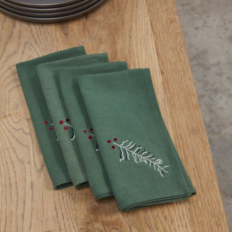 Set of green embroidered napkins on a wooden table with dark plates in the background.
