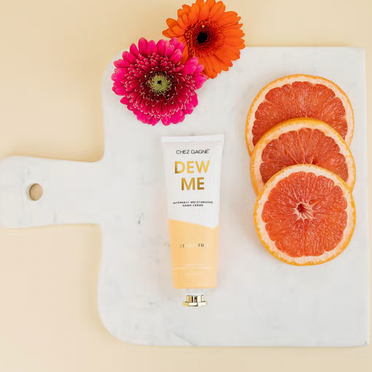 Chez Gagne Dew Me Grapefruit hand lotion displayed with Grapefruit slices, on cutting board and Flowers  