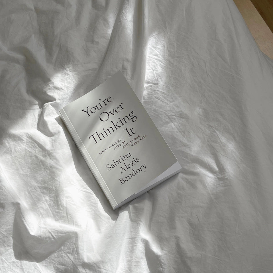 Book titled 'You're Over Thinking It' by Sabrina Alexia Bendory on a white fabric surface.
