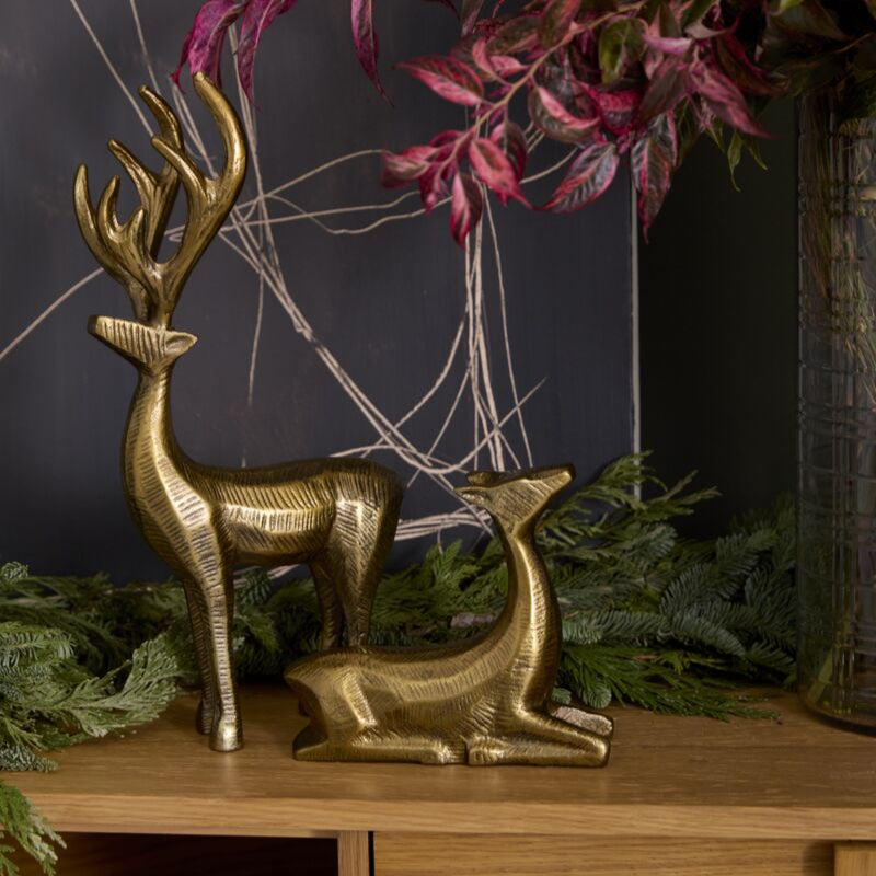 Gold deer figurines on a wooden surface with greenery and a dark background