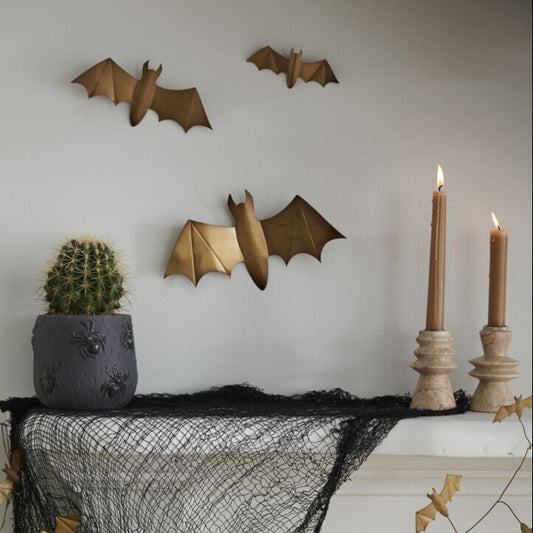 Halloween-themed decor with black netting, gold bats, and candles on a white surface.